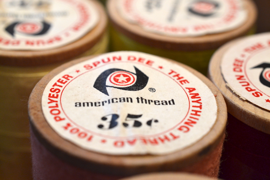 A close up photo of a thread spool whose label says: "100% Polyester - Spun Dee - The Anything Thread" with a center section that shows the American Thread trademark logo and the words "American Thread" and a price of 35 cents.