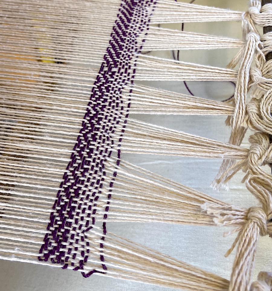 A closeup image of a loom showing warp and weft fibers being woven